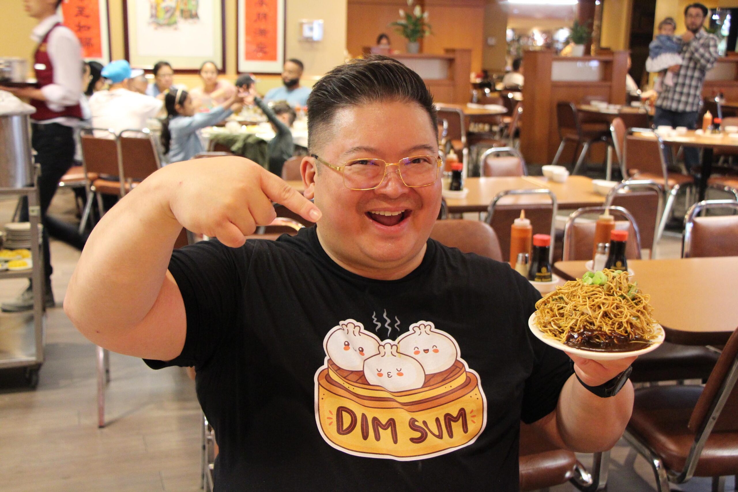Carter Chen poses next to a plate of noodles at a Dim Sum tour